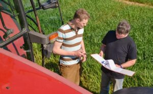 Ein Landwirt erklärt einem Auszubildenden auf dem Feld neben einem Traktor